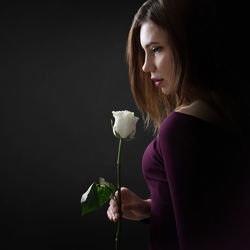 Side view of woman holding white rose against black background