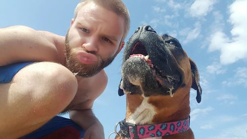 Low angle view of man puckering by dog against sky