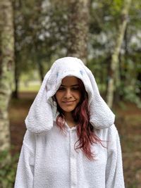 Young woman wearing white warm clothing while standing against trees