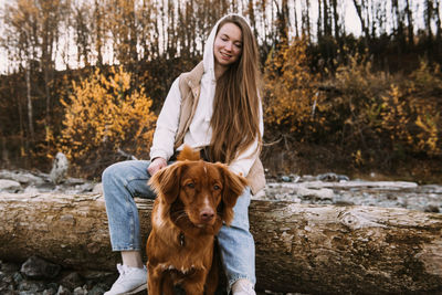 Young woman and dog retriever walks on river shore at autumn season