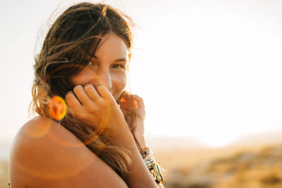 Portrait of young woman smiling while standing at beach during sunset
