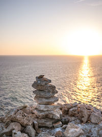 Stack of rocks at sea shore against sky during sunset