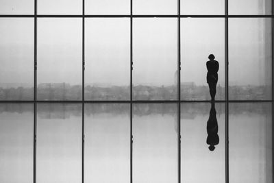 Rear view of woman standing against glass window in modern building