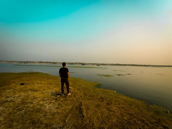 Rear view of man standing on beach against sky