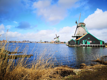 Traditional windmill by water against sky