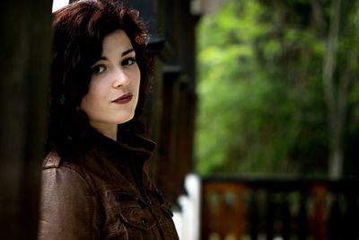 Close-up portrait of young woman standing against tree trunk