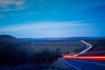 Light trails on road against blue sky