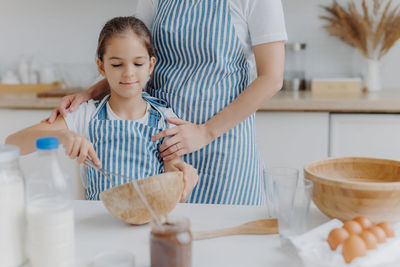 Midsection of mother standing with daughter mixing in bowl on table