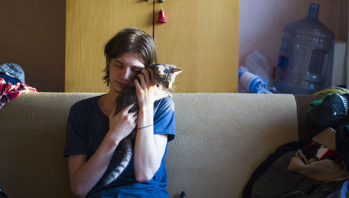 Young man embracing cat while sitting on sofa at home