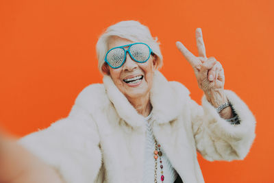 Portrait of smiling senior woman against orange background