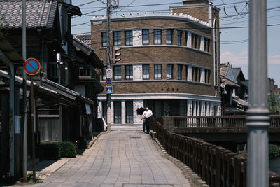 Rear view of man walking on street amidst buildings