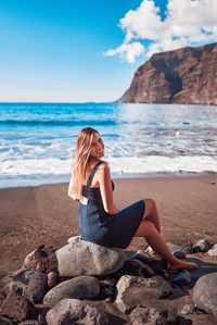 Woman sitting on rock at beach against sky