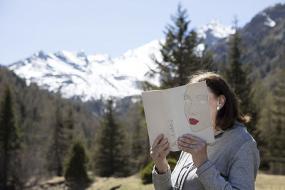 Woman covering face with book, reading poetry in the mountains