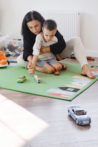 Disabled boy playing toy cars with mother at home. cerebral palsy child entertaining on the mat