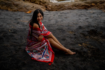 Portrait of young woman with shawl sitting on black sand beach