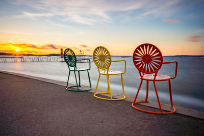 Deck chairs on beach against sky during sunset