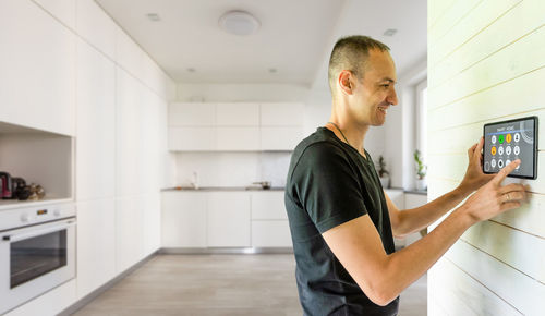 Side view of young man using mobile phone while standing at home