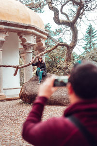 Man photographing woman sitting on rock against gazebo