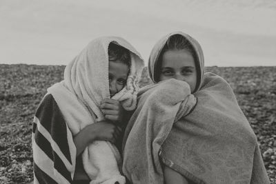 Portrait of brother and sister covered with towels at beach