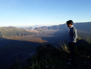 Side view of man standing on mountain against clear blue sky