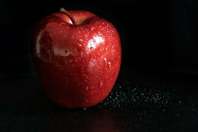 Close-up of wet apple on table against black background