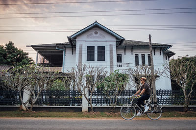 People riding bicycle on house by building against sky