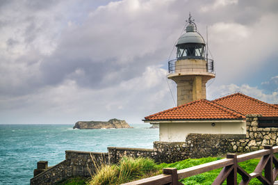 Lighthouse by sea and buildings against sky