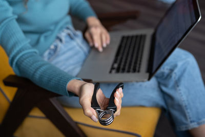 Female office worker using laptop and compressing adjustable hand carpal expander simulator