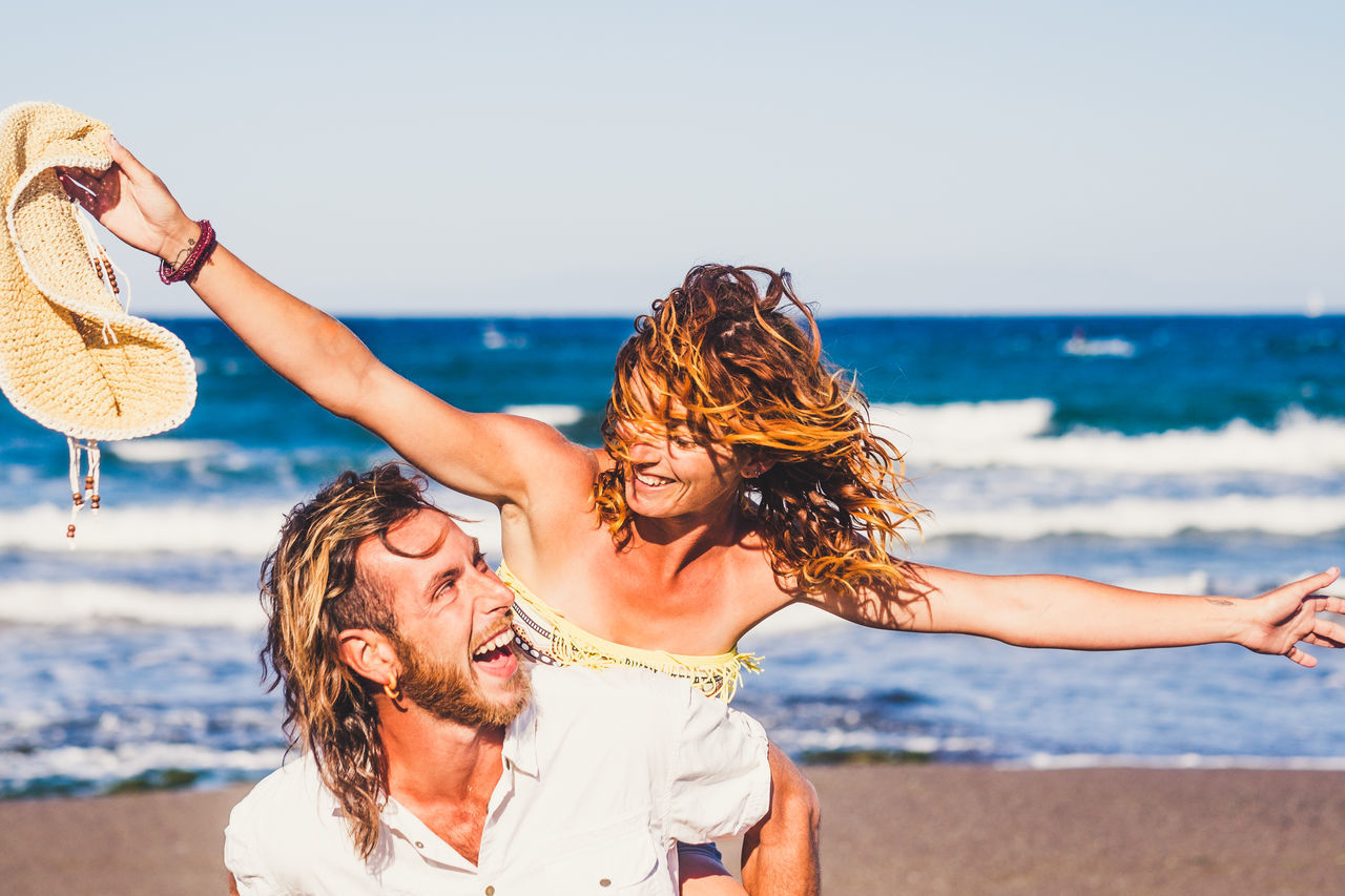 MIDSECTION OF COUPLE ON BEACH AGAINST SEA