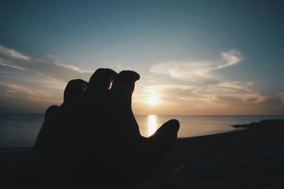 Silhouette hand on beach against sky during sunset