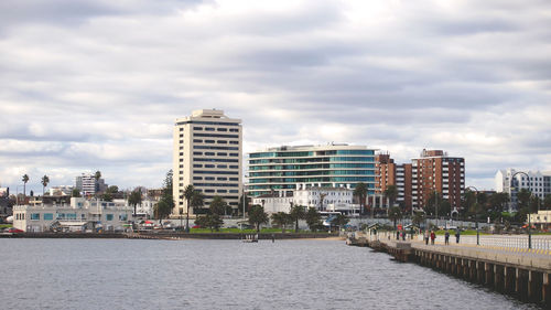 Modern cityscape by sea against sky