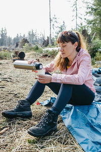 Young beautiful woman drinking hot tea or coffee from a thermos in the forest on a walk. hiking