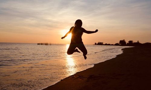 Full length of silhouette woman jumping at beach against sky during sunset