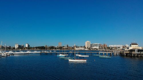 Boats sailing in river against clear blue sky