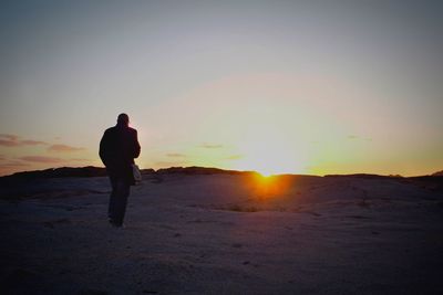 Rear view of man walking on field against sky during sunset