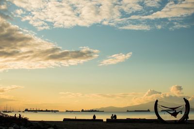 Silhouette people on beach against sky during sunset