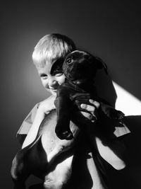 Portrait of boy holding puppy against wall