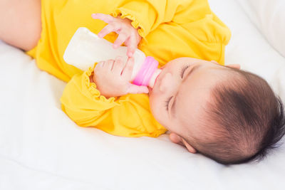 High angle view of baby girl drinking milk on bed