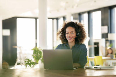 Portrait of smiling young woman using phone while sitting on table