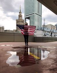 Woman with umbrella flag in city against sky