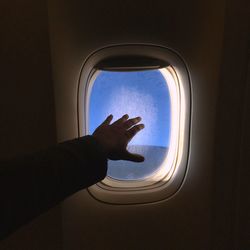 Cropped hand of person gesturing by airplane window