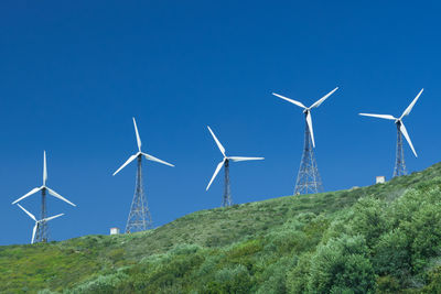 Low angle view of wind turbines on landscape against clear blue sky