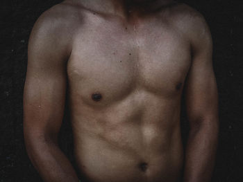 Midsection of shirtless man standing against black background