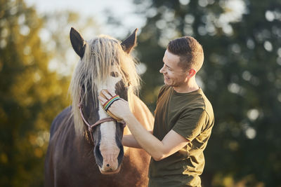 Man during grooming horse on sunny summer day. close-up of hand while brushing of horse.