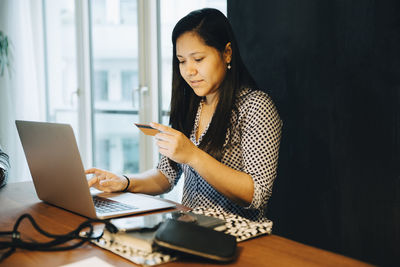 Young woman using phone while sitting on table