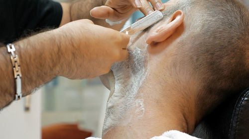 Barber doing shaving of mature man in salon