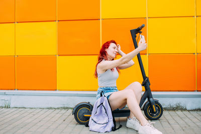 Woman uses a smartphone and an electric scooter in the summer in the city