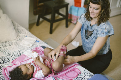 Mother adjusting diaper of daughter lying on baby carrier at home