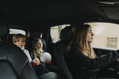 Mother driving while son and daughter sitting behind in car during weekend trip
