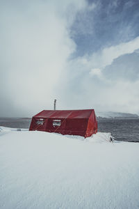 Built structure on snow covered land by sea against sky